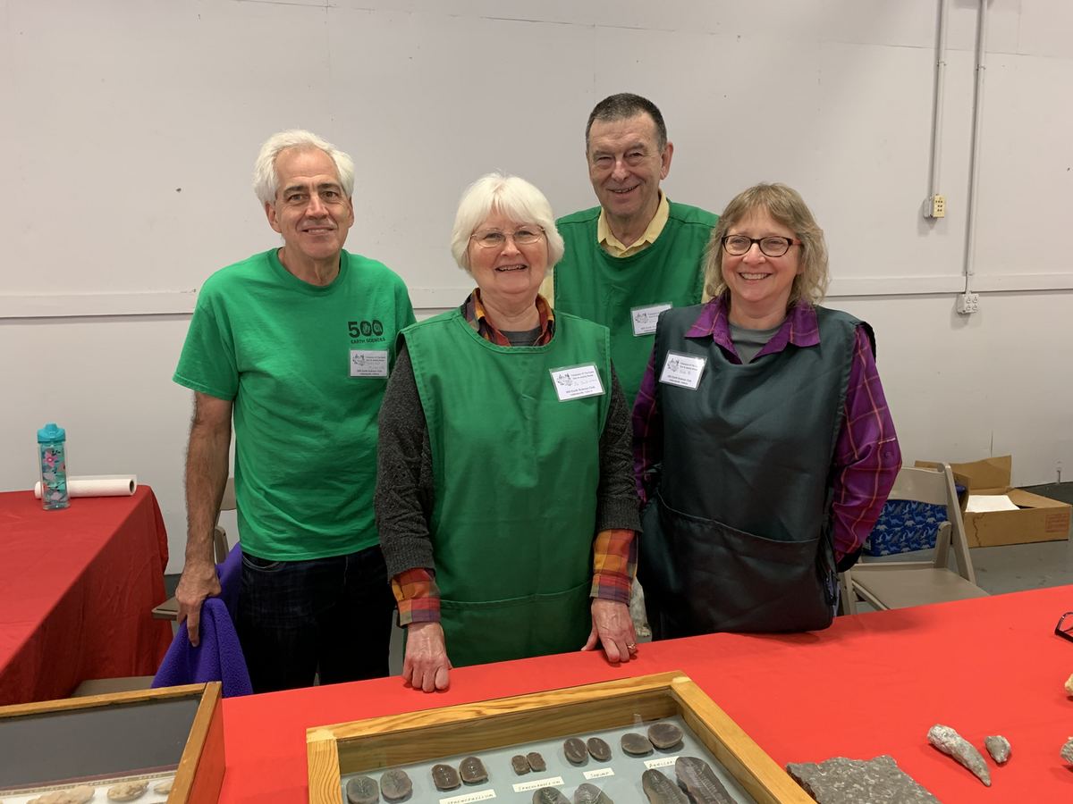 Four club members standing behind a display table of Indiana fossils at an outreach event